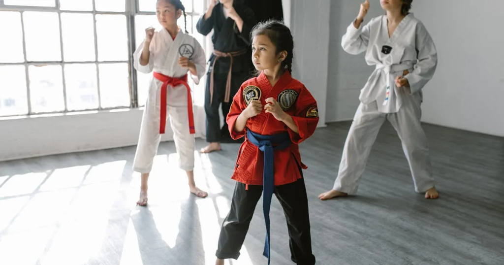 Three martial arts students in uniform and a trainer teaching a child a pose in a dojo