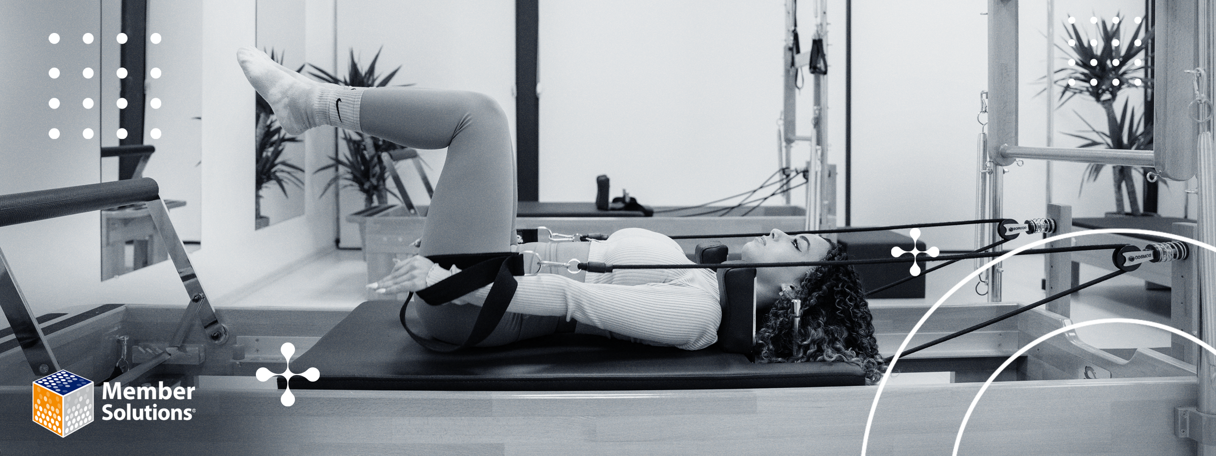 A woman uses a Pilates reformer, lying on her back with raised legs, in a calm studio setting