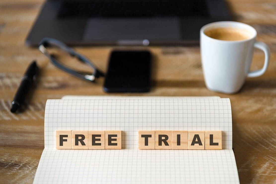 Free Trial tile letters on top of notepad with coffee and office items on desk.