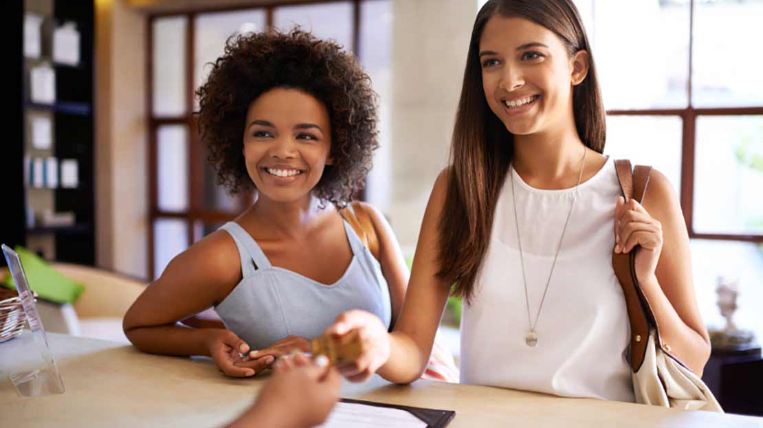 Two young women hand credit card for membership payment to representative at front desk