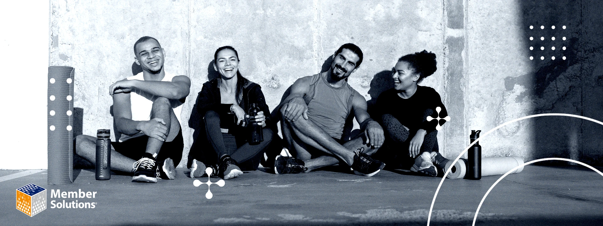 Four groups of men and women are sitting against a wall, smiling, with some fitness training equipment beside them