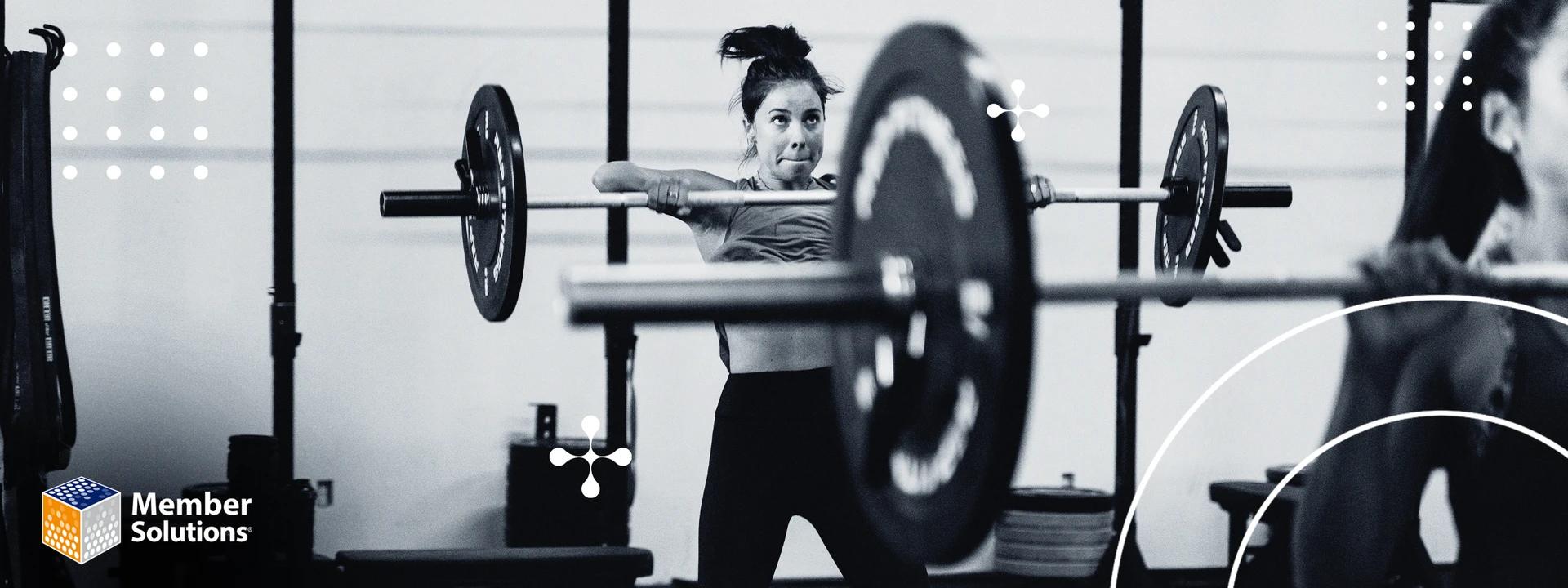 A woman performing a clean lift with a barbell in a gym, looking focused and determined