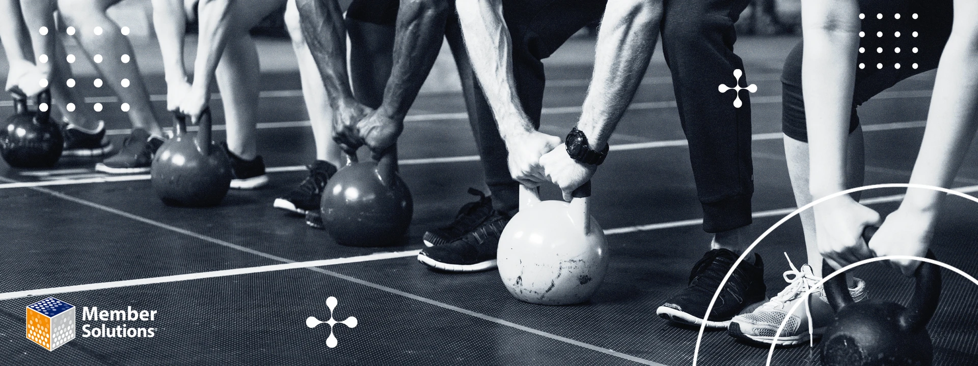 A group of people, seen from the waist down, gripping kettlebells on a gym floor, conveying strength and determination