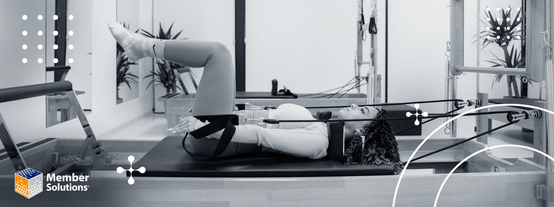 A woman uses a Pilates reformer, lying on her back with raised legs, in a calm studio setting