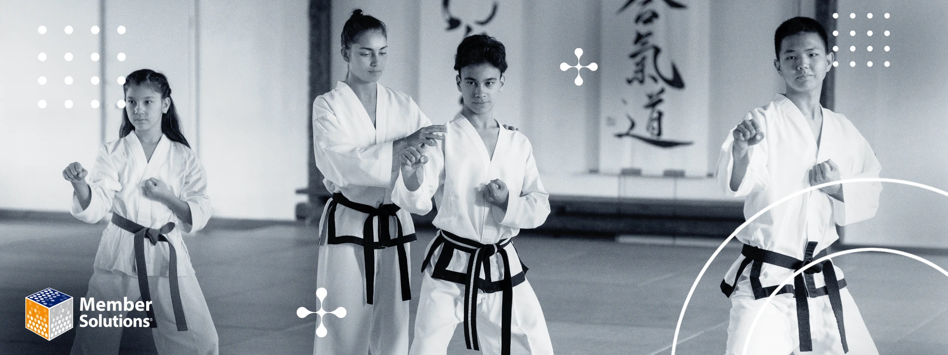 Three martial arts students in uniform and a trainer teaching a child a pose in a dojo